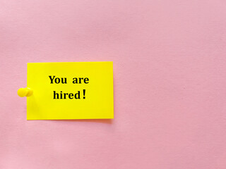 You are hired text written  on sticky note on pink background . Top view with copy space 
