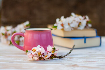 a pink cup and a blossoming twig of an almond tree on a table next to books