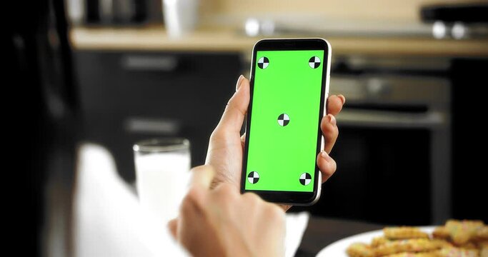 Close-up. A woman is sitting with her back in the kitchen, holding a smartphone with a green screen, using a new mobile application, swiping her finger from top to bottom on the phone screen.Chromakey