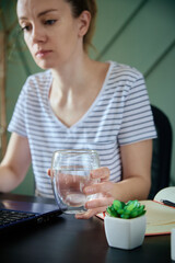 Woman holds glass of water while working remotely at home office, Healthy care for freelancer work