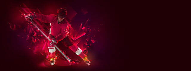 Young man, professional hockey player in protective uniform training isolated on dark background...