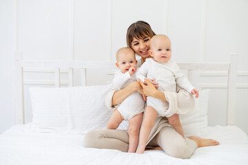 Fototapeta na wymiar happy mom with two twin babies at home on the bed hugging and kissing, happy young family with children, motherhood