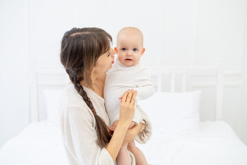 happy mom with a baby daughter at home on the bed hugs and kisses, happy young mother and motherhood