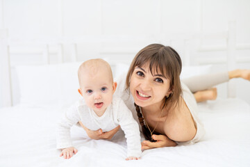 happy mom with a baby daughter at home on the bed hugs and kisses, happy young mother and motherhood