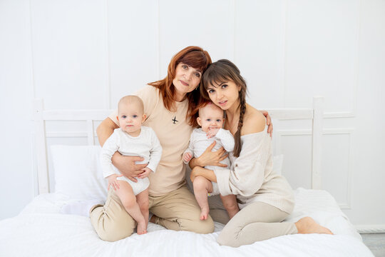 Mom With Two Twin Babies And Grandma At Home On The Bed Hugging And Kissing, Happy Family,