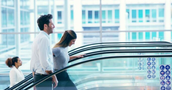 On their way up. Two young businesspeople going up the escalator in an airport. Two working colleagues traveling to a conference. Businessman and businesswoman on their way to a meeting. 