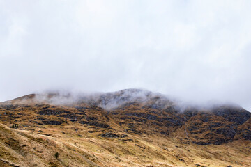 Low clouds floating above the mountainous landscape of the Highlands, stunning scenery with barren summits, steep glens and small waterfalls caused by the persistent rain, Argyll Forest Park, Scotland