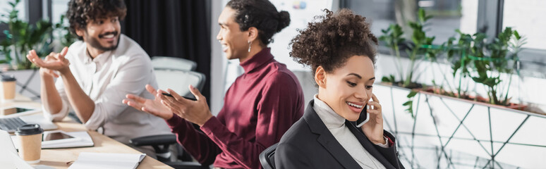 Cheerful african american businesswoman talking on cellphone in office, banner.