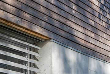 Detal architektoniczny na fragment elewacji domu jednorodzinnego wykonanego z drewna i betonu. Widoczne okno z żaluzjami aluminiowymi elewacyjnymi - obrazy, fototapety, plakaty