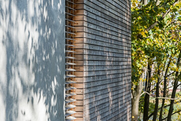 Detal architektoniczny na fragment elewacji domu jednorodzinnego wykonanego z drewna i betonu. Widoczne okno z żaluzjami aluminiowymi elewacyjnymi - obrazy, fototapety, plakaty