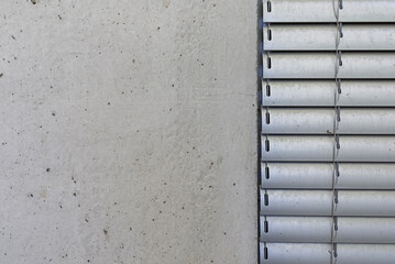 Detal architektoniczny na fragment elewacji domu jednorodzinnego wykonanego z betonu. Widoczny fragment żaluzji aluminiowych elewacyjnych.