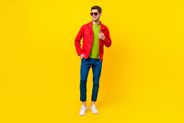 Fototapeta na wymiar Full length photo of funky brunet millennial guy look empty space wear glasses shirt pants sneakers isolated on yellow background