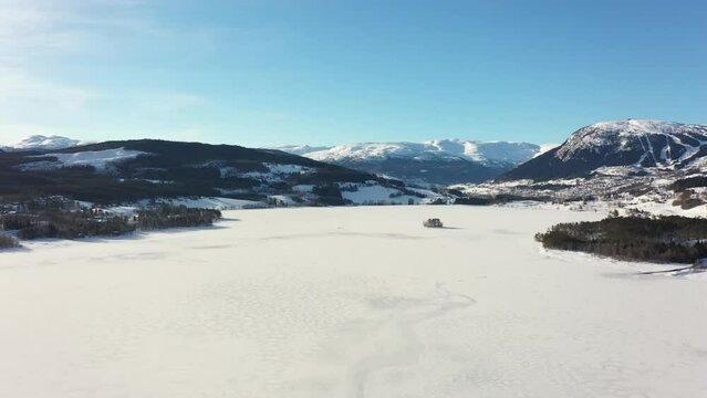 Reverse aerial over frozen massive lake Tunhovdfjorden in Norway with mountain Dyna and Myking in background