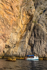 : Black Sea red rocks coastline. Coastal red rocks, boat and blue sea. Seascape. Summer. Traveling.