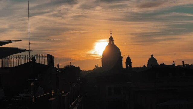 Wide shot showing silhouette of famous Bas&iacute;lica de San Pedro during golden sunset in backdrop - Vatican City