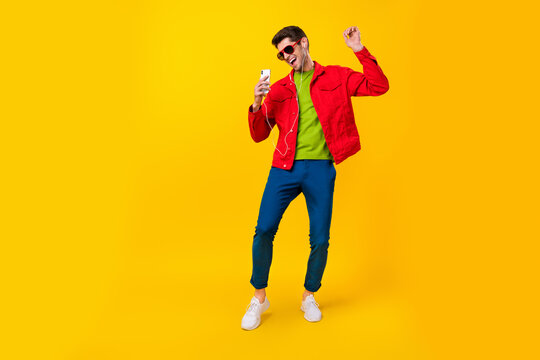 Full size photo of impressed millennial guy dance listen music wear glasses jacket jeans footwear isolated on yellow background