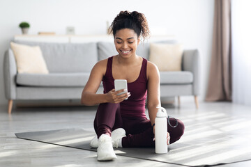 Happy athletic black woman using mobile phone while exercising