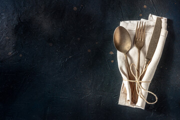Cutlery. A spoon, a fork, and a knife in a napkin on a black background. Modern silverware on a...