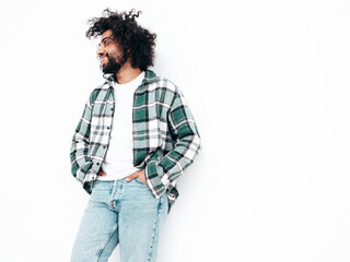 Handsome smiling hipster  model.Sexy unshaven Arabian man dressed in summer shirt and jeans clothes. Fashion male with long curly hairstyle posing near white wall in studio. Isolated