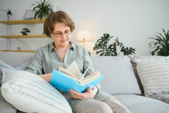 Old lady sitting on couch and enjoying interesting novel stock photo