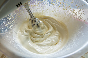 A close-up of cream is being whisked with an electric whipping machine. Motion blur as whisks are rotating at high speed.