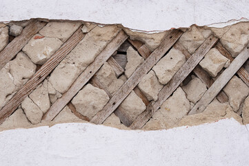 Fragment of the destroyed wall of an old house. Ancient construction technologies. Concrete and wooden slats.