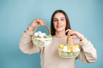 Cute brunette woman holds painted Easter eggs in baskets in her hands, Easter, in the studio on a blue background.