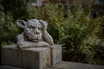 Closeup of a statue of a gargoyle or a gordon with its hand on the head in a park or garden - obrazy, fototapety, plakaty