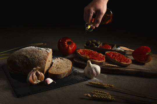 Unrecognizable person pouring oil on bread with tomatoes