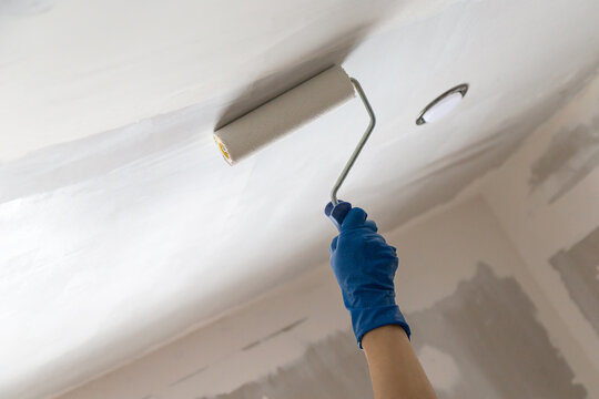 A worker applying whitewash on the ceiling using a handle roller at home
