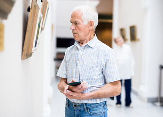 mature European man examines paintings in an exhibition in hall of an art museum