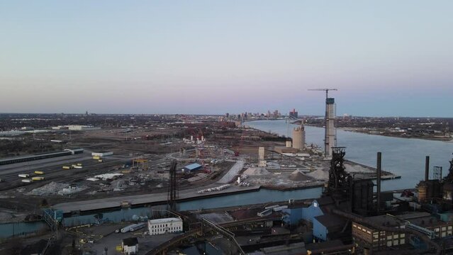 Aerial flyover of Industrial structures with cranes and towers at Detroit river and skyline in the background, Michigan.