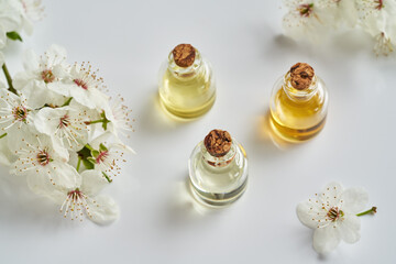 Obraz na płótnie Canvas Essential oil bottles with white blossoms in springtime on bright background