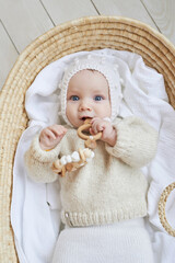 Fototapeta na wymiar Baby in wicker cradle with wooden toy. Mothers Day. Children Protection Day. Cheerful child, happy childhood