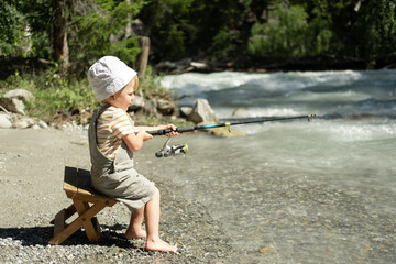 little child boy fishing with a fishing rod on the mountain river on summer day