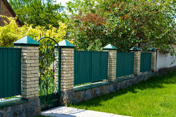 Green metal corrugated fence and gate with brick pillars on a green background.