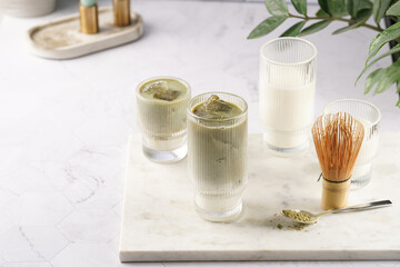 tall rippled glass with matcha latte - japanese green tea powder and whipped milk on marble board in white kitchen