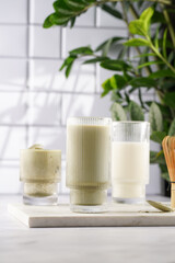 tall rippled glass with matcha latte - japanese green tea powder and whipped milk on marble board in white kitchen