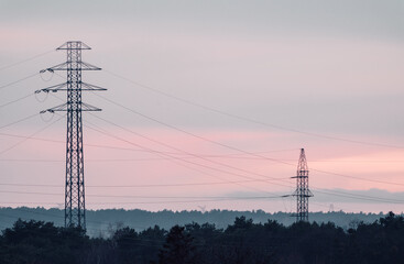 High voltage poles connected by cables against a sky colored by a red sunset