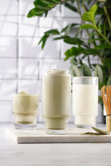 tall rippled glass with matcha latte - japanese green tea powder and whipped milk on marble board in white kitchen
