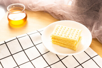 Closeup of crispy crackers on the white plate and a cup of green tea on the wooden shelf