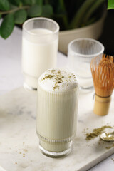 tall rippled glass with matcha latte - japanese green tea powder and whipped milk on marble board in white kitchen
