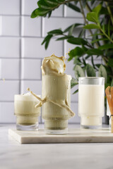 tall rippled glass with matcha latte with splashes - japanese green tea powder and whipped milk on marble board in white kitchen