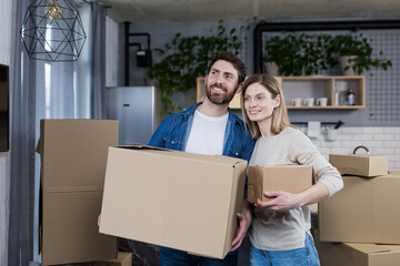 Happy couple man and woman live together, moved to a new rented apartment, holding cardboard boxes