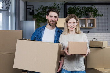 Happy family, man and woman together in a new apartment looking at the camera and smiling holding cardboard boxes, housewarming