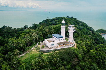 Bird's eye view of a lighthouse on top of a mountain covered with green trees against the sea