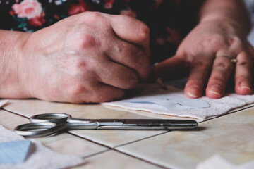 The hands of an elderly woman cut out details for sewing a child's toy. Sewing toys. Hobby. Sewing and cutting of soft fabric. handicraft at home. Elderly woman sew the details of a toy.