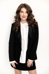 A pensive young business woman in stylish suit stands in the studio. Female posing for the camera, looking to the side against black background. A beautiful girl is thinking about career success.