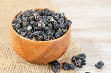 Fototapeta na wymiar Black wolfberries or black goji berries, in a wooden bowl on table.