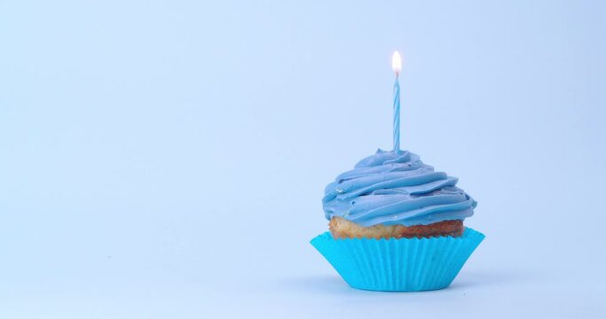 Delicious cupcake on light blue background. Woman lighting candle, closeup